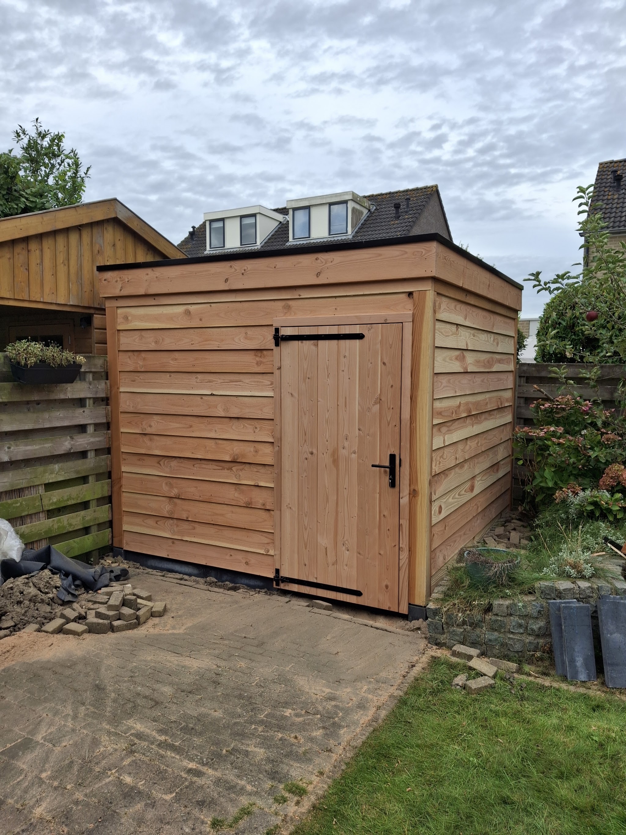 Nieuwe houten schuur met horizontale delen en een deur, in een tuin