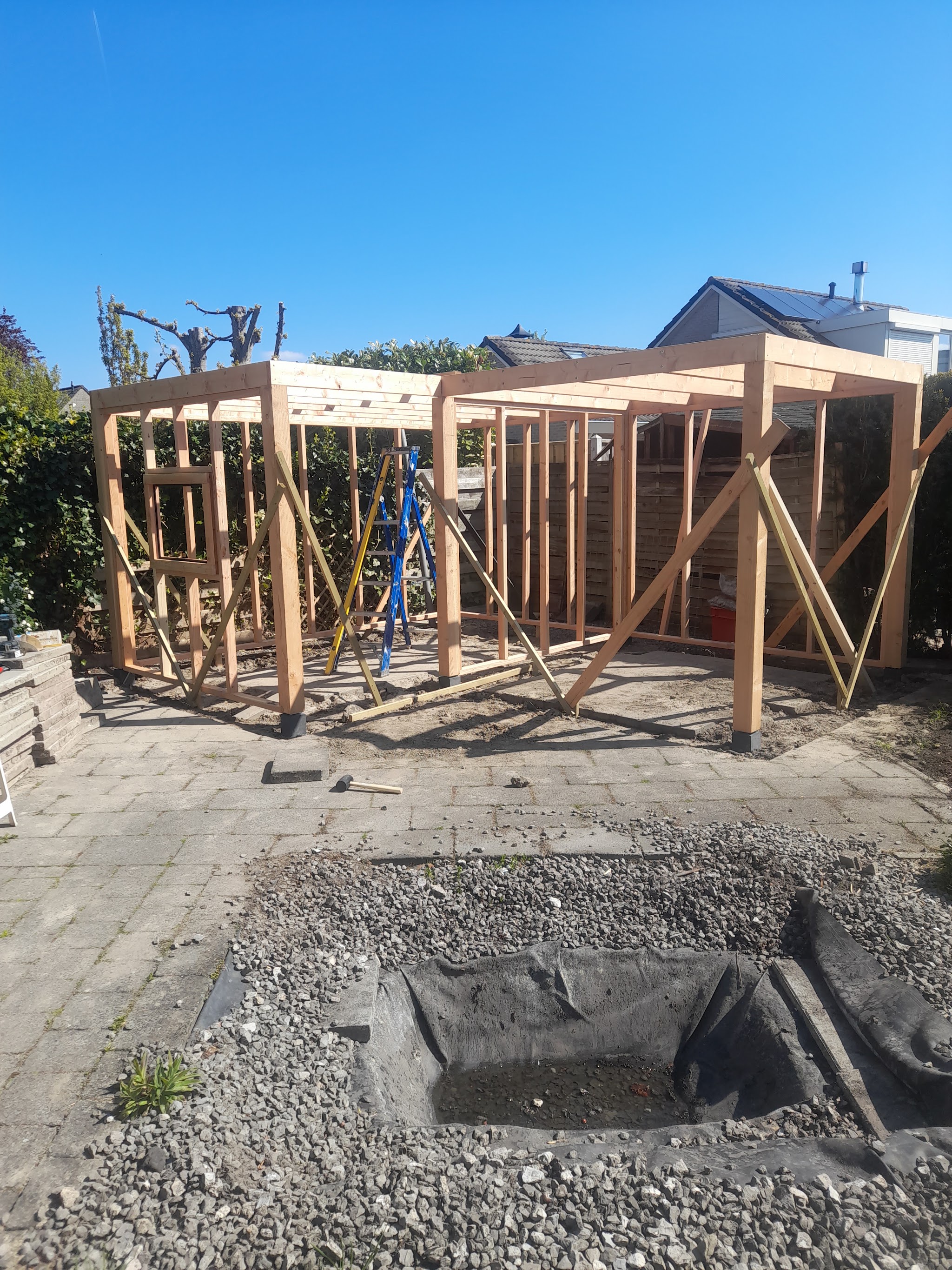 Het houten frame van een overkapping in aanbouw, onder een blauwe lucht