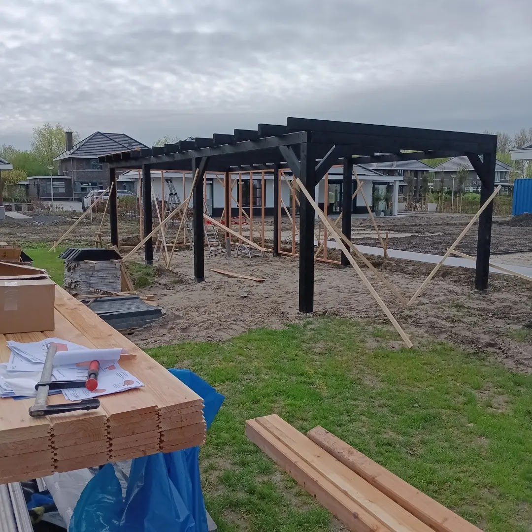 Zwarte pergola in aanbouw in een nieuwe tuin, met hout op schragen ervoor