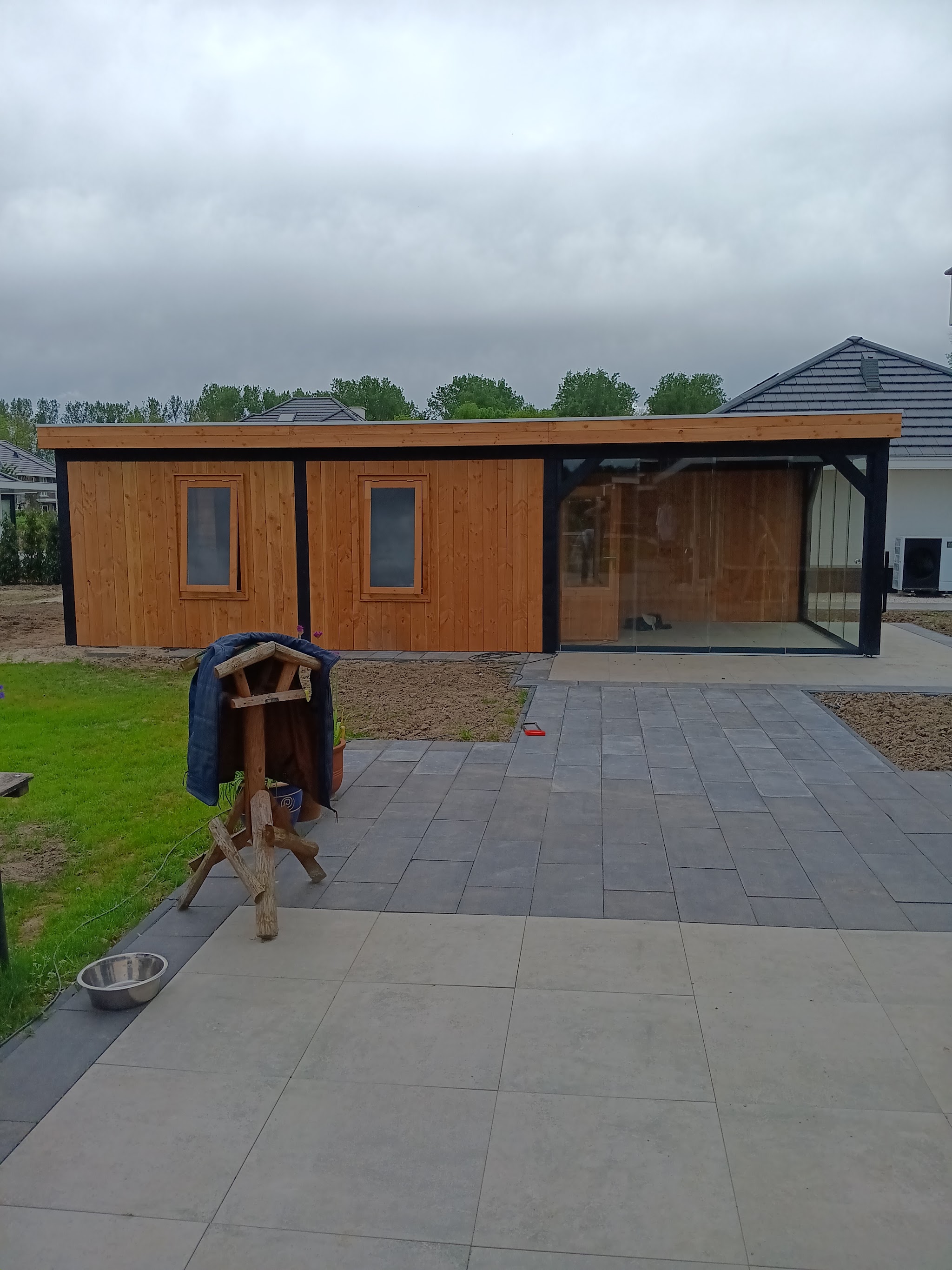 Lange houten tuinkamer met ramen en een glazen deel, terras ervoor